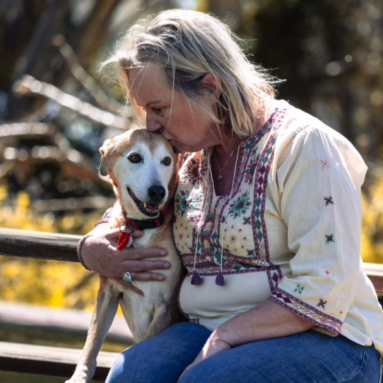 Woman kissing her dog on a park bench, showing the bond that highlights the importance of keeping pets with their families