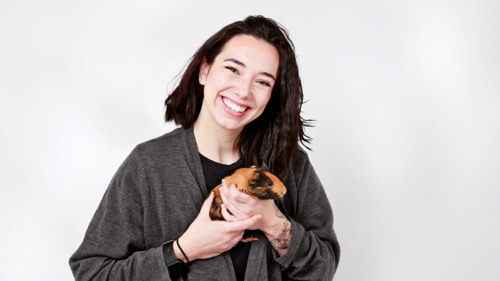 Brennan with hair shoulder length hair smiles while holding a guinea pig in her hands and talks about compassion fatigue. 