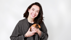 Brennan with hair shoulder length hair smiles while holding a guinea pig in her hands and talks about compassion fatigue.