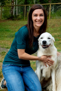 Dr. Katie Gray, DVM kneels next to white dog in open field.