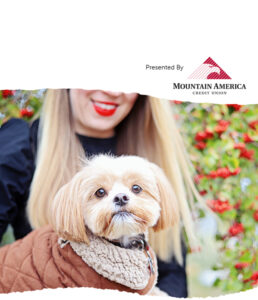 woman with red lips holding a maltese mix dog in front of red berry bush
