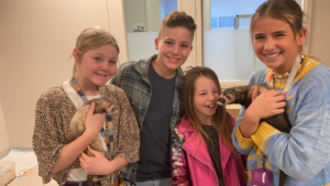 Olivia, a seventh-grade student stands with 3 friends, all smiling while holding two ferrets.