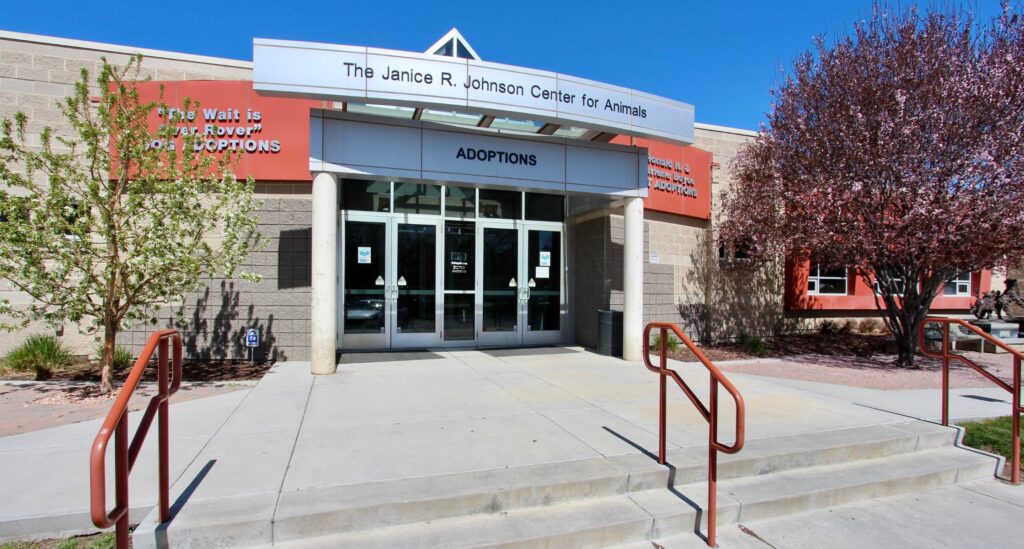 The front entrance to the Humane Society of Utah's Adoption Center with blue skies and pink flowering trees in front of building. 