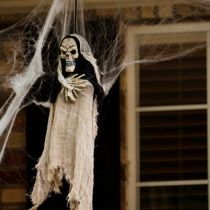 A scary looking skeleton ghost dangles from a front porch with cobwebs around it.