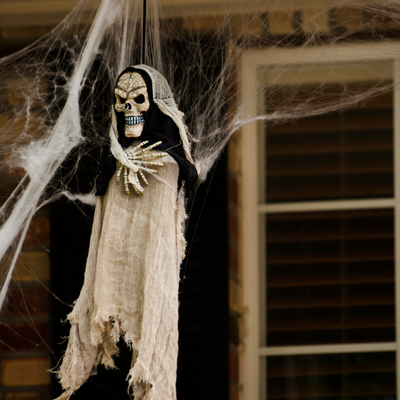 A scary looking skeleton ghost dangles from a front porch with cobwebs around it. 